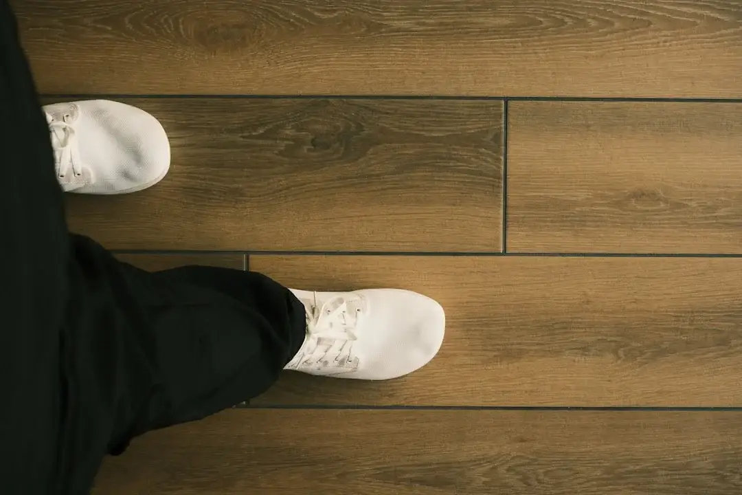 Pieds chaussés de baskets blanches sur un large plancher de bois franc brun