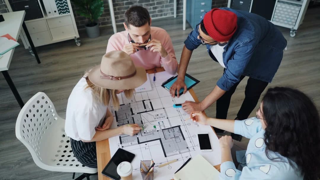 Équipe de professionnels qui examinent des plans architecturaux ensemble autour d'une table dans un bureau moderne