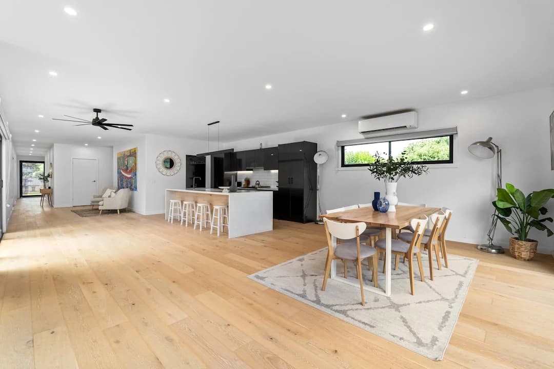 Grand espace ouvert rénové avec plancher de bois clair, cuisine noire et salle à manger lumineuse