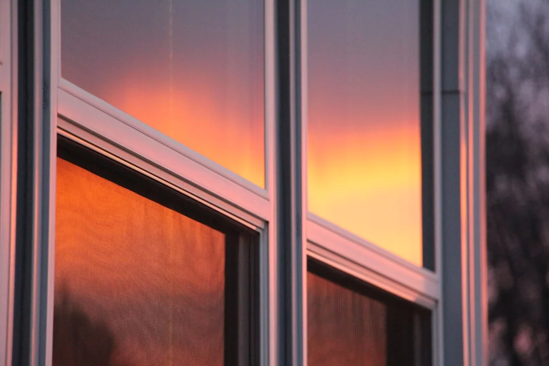 Gros plan sur des cadres de fenêtres blancs reflétant un coucher de soleil orange et rose