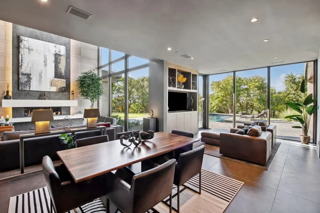 Modern living and dining room with floor-to-ceiling panoramic windows, fireplace, and solid wood dining table