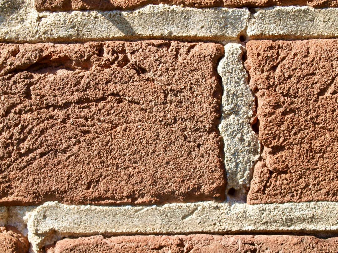 Gros plan sur des briques rouges anciennes aux joints de mortier larges et texturés, maçonnerie patrimoniale à la chaux