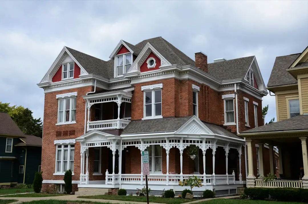 Maison victorienne en brique rouge avec galerie ornée de dentelle de bois blanche, architecture patrimoniale