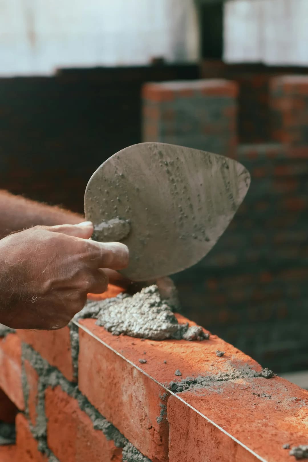 Craftsman's hand holding a masonry trowel with fresh grey mortar, repointing a brick wall
