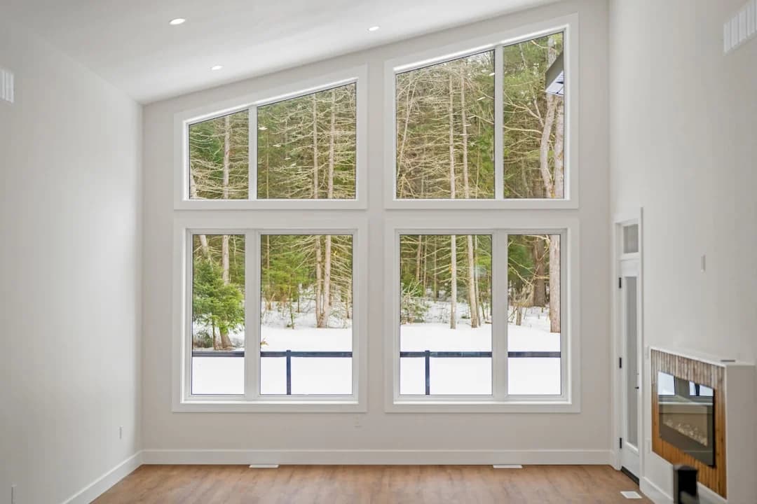 Salon moderne avec de grandes fenêtres blanches donnant sur une forêt enneigée