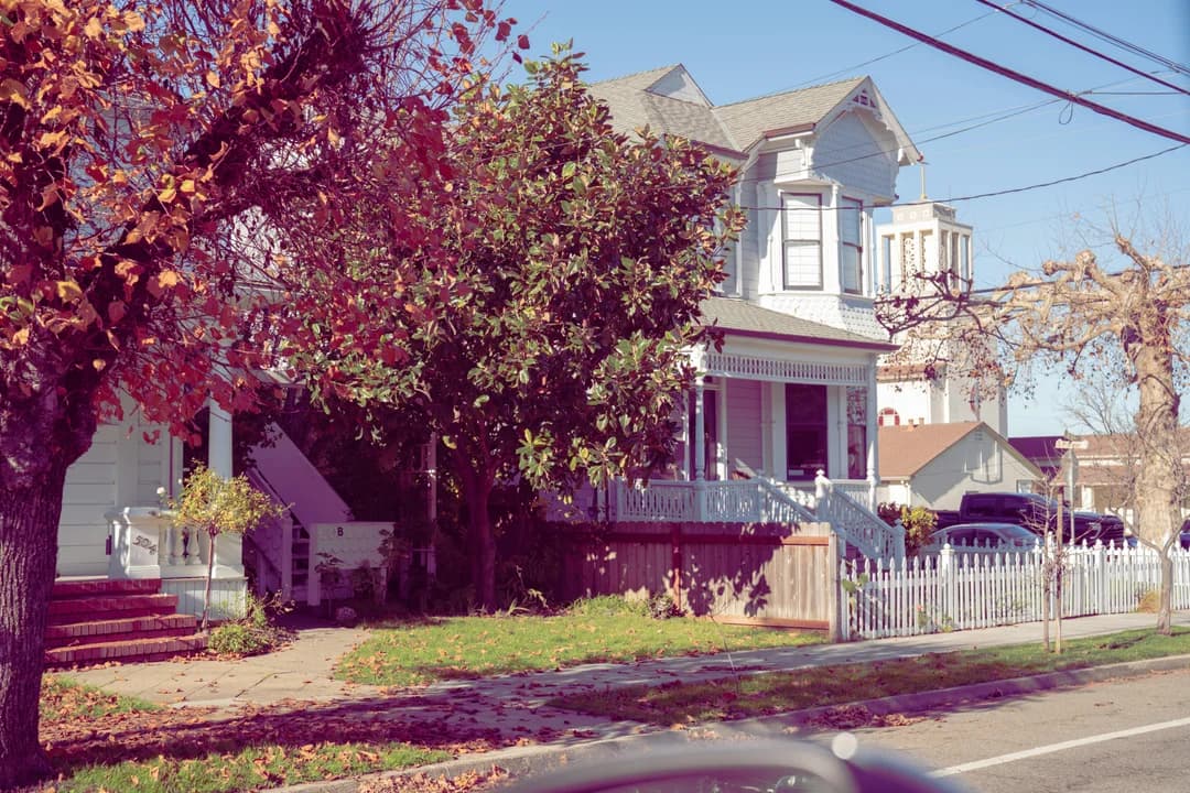 Victorian house with white picket fence and autumn foliage on a residential street